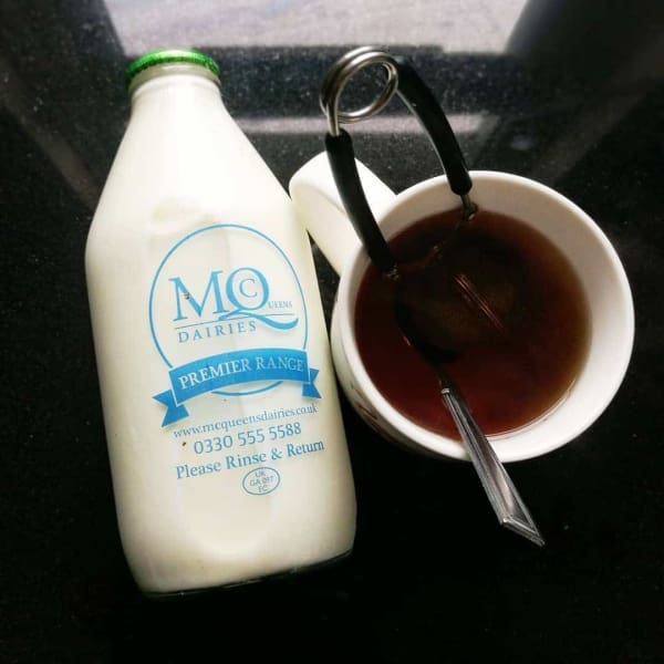 Glass milk bottle beside cup of tea