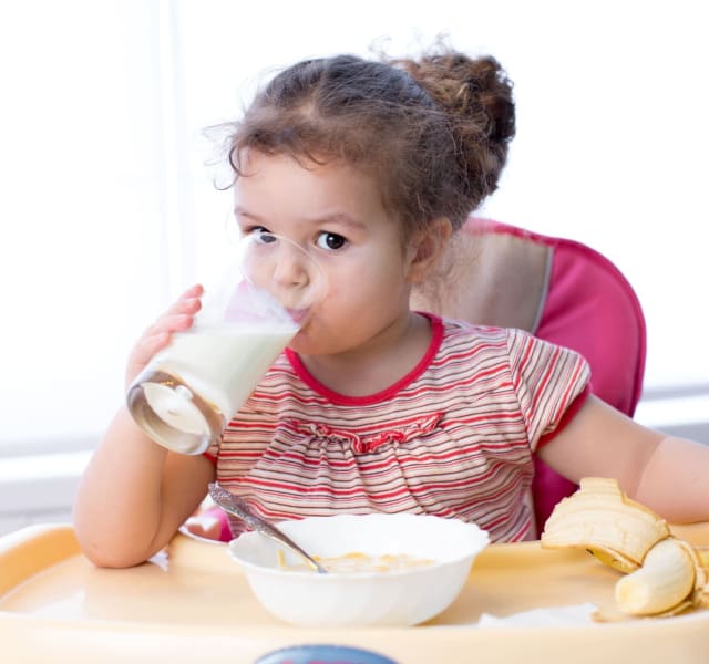 Young child drinking a glass of milk and benefiting from the Nursery Milk Scheme